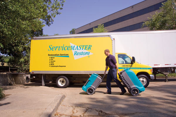 ServiceMaster Water restoration technician with his equipment moving towards the Van